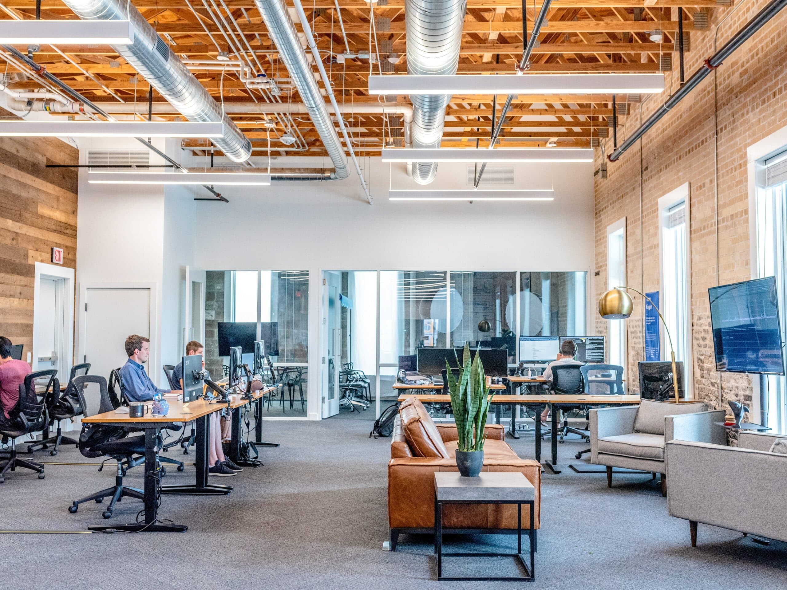 Grande pièce au style industriel dans laquelle sont installés de nombreux bureaux et des canapés